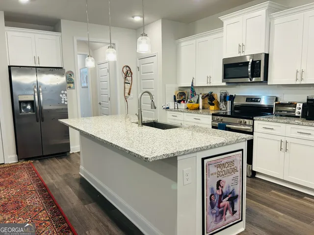 a kitchen with stainless steel appliances granite countertop a refrigerator a stove and a sink with wooden floor