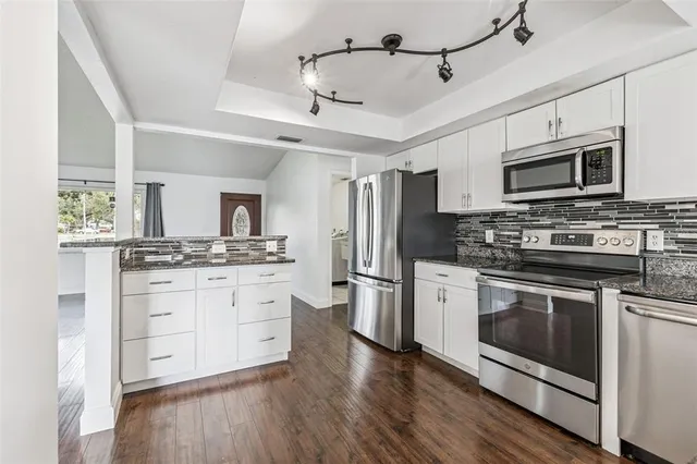 a kitchen with stainless steel appliances white cabinets a sink a stove a microwave and wooden floors