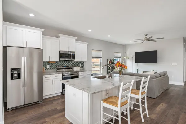 a kitchen with stainless steel appliances granite countertop a stove top oven a refrigerator a kitchen island a dining table and chairs with wooden floor