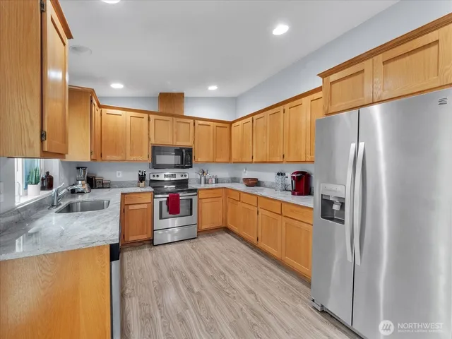 a kitchen with stainless steel appliances granite countertop a refrigerator a stove top oven a sink and dishwasher with wooden floor