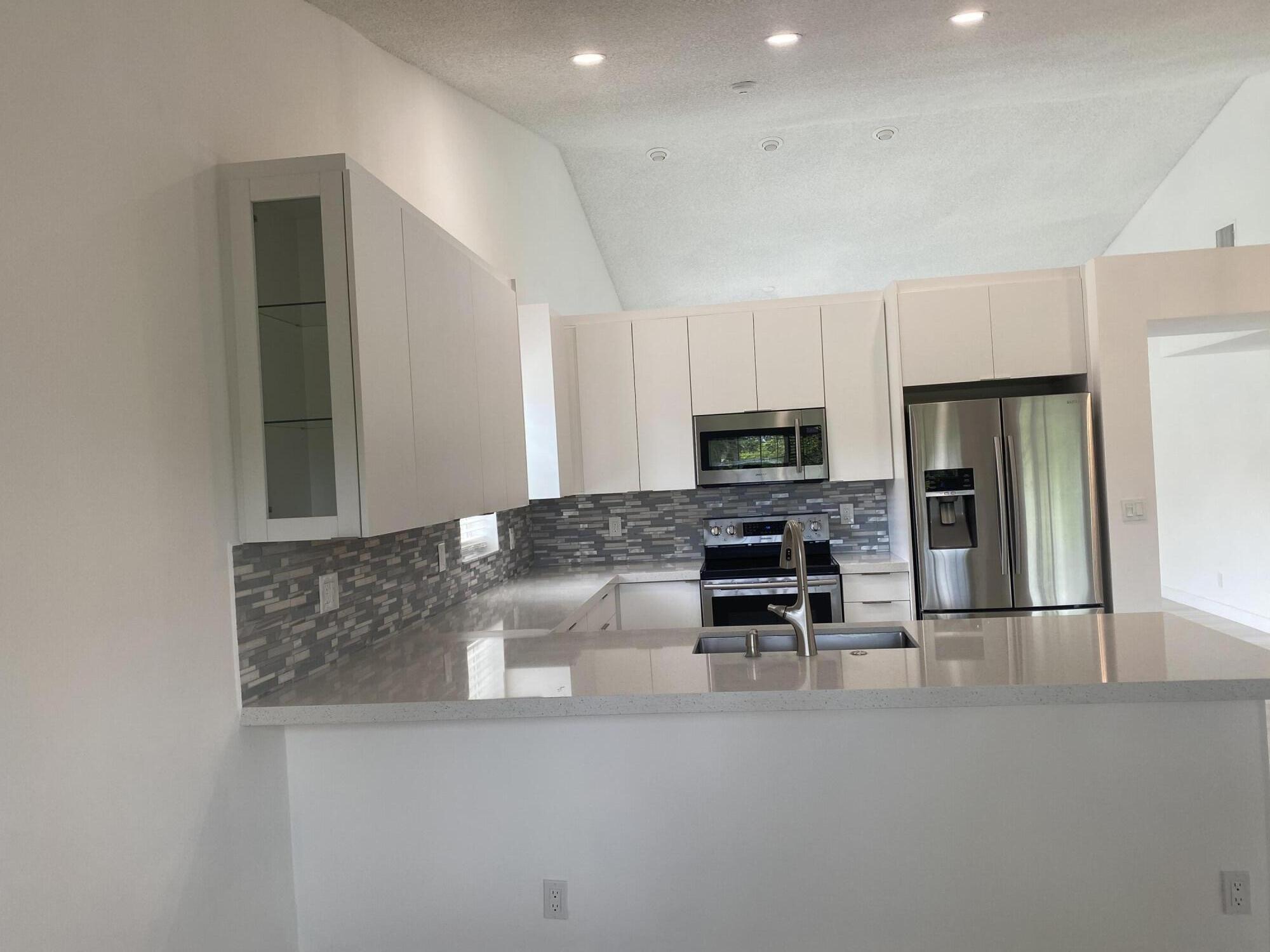 7591 Red Ruby Drive Delray Beach, FL 33446 - Photo 12 of 29 a kitchen with stainless steel appliances granite countertop a stove top oven a sink a refrigerator and white cabinets
