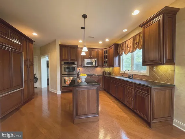 a kitchen with stainless steel appliances granite countertop a refrigerator a sink dishwasher and wooden cabinets with wooden floor