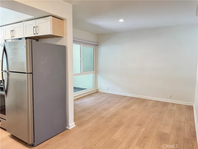 a view of a refrigerator in kitchen and an empty room with wooden floor