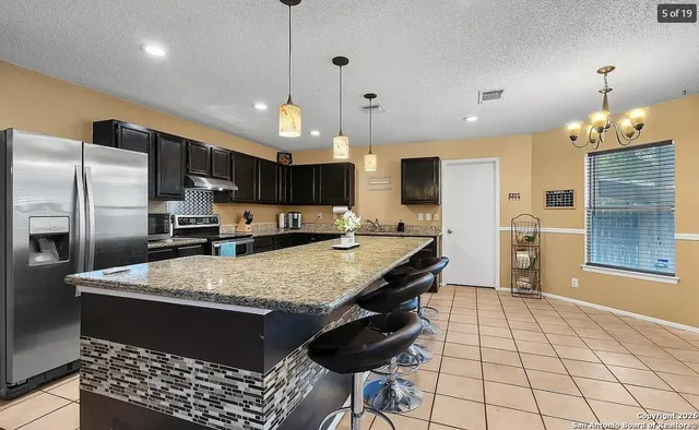 a large kitchen with stainless steel appliances kitchen island granite countertop a table chairs and a refrigerator
