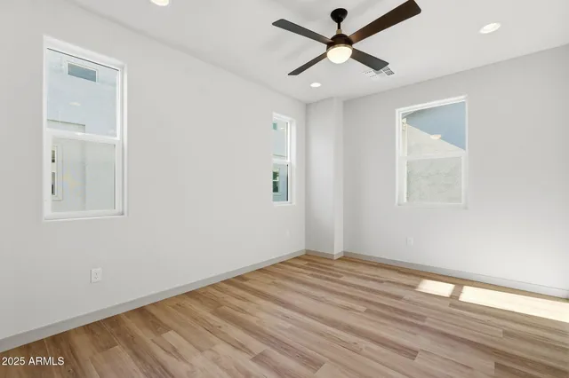an empty room with wooden floor ceiling fan and windows