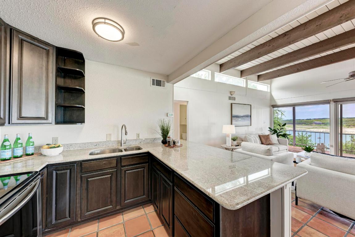 8130 Joy Road Volente, TX 78641 - Photo 17 of 36 Kitchen with dark brown cabinets, light stone countertops, a water view, beam ceiling, and a peninsula