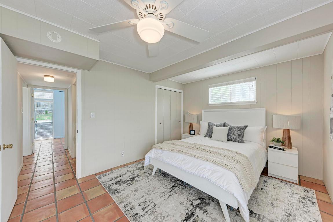 8130 Joy Road Volente, TX 78641 - Photo 21 of 36 Bedroom with multiple windows, light tile patterned floors, wood walls, a ceiling fan, and a closet