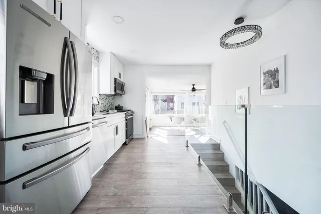 a large white kitchen with stainless steel appliances a stove a chimney a sink and cabinets