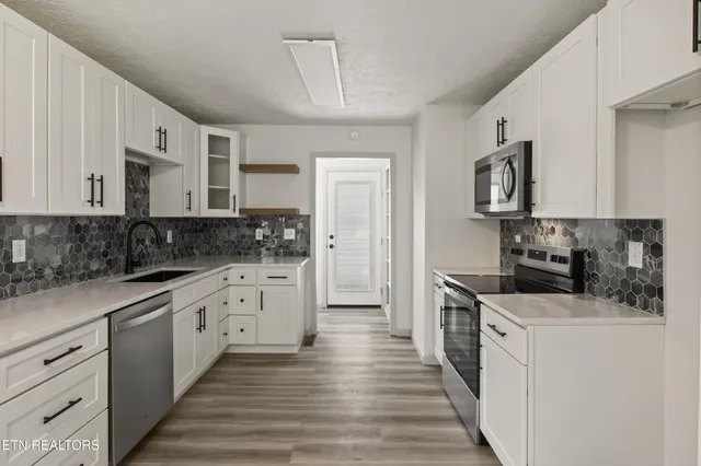 a kitchen with stainless steel appliances granite countertop a stove top oven a sink a refrigerator white cabinets and wooden floor