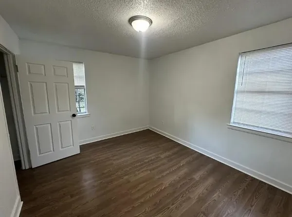 an empty room with wooden floor chandelier fan and windows