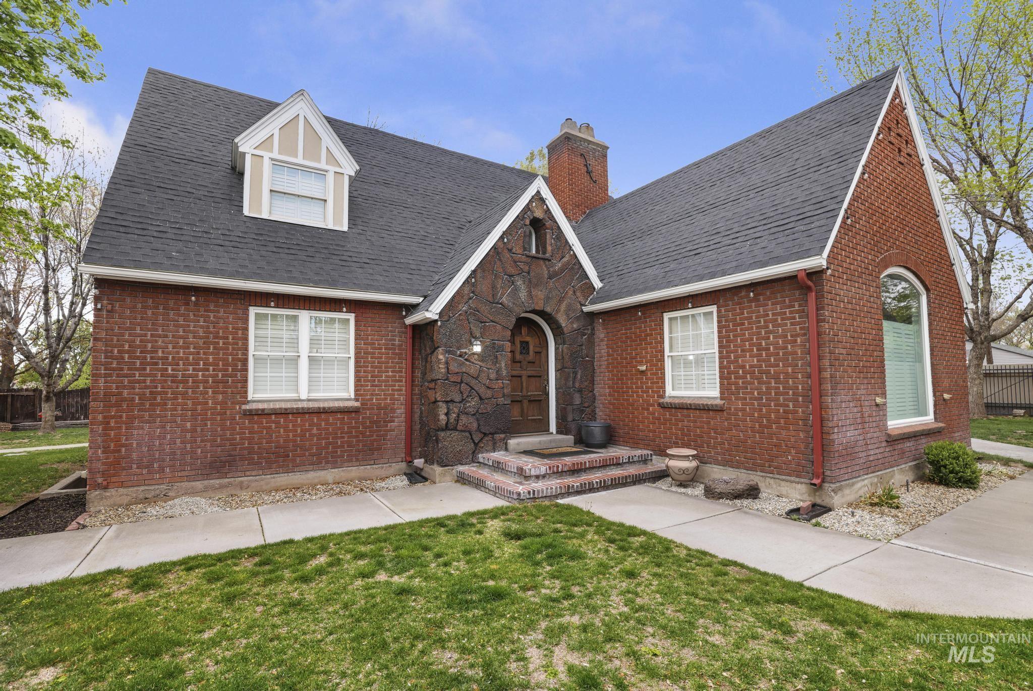 Brick residence featuring a stone-clad entry, dark shingle roof, arched front door, prominent dormer window, and an arched window