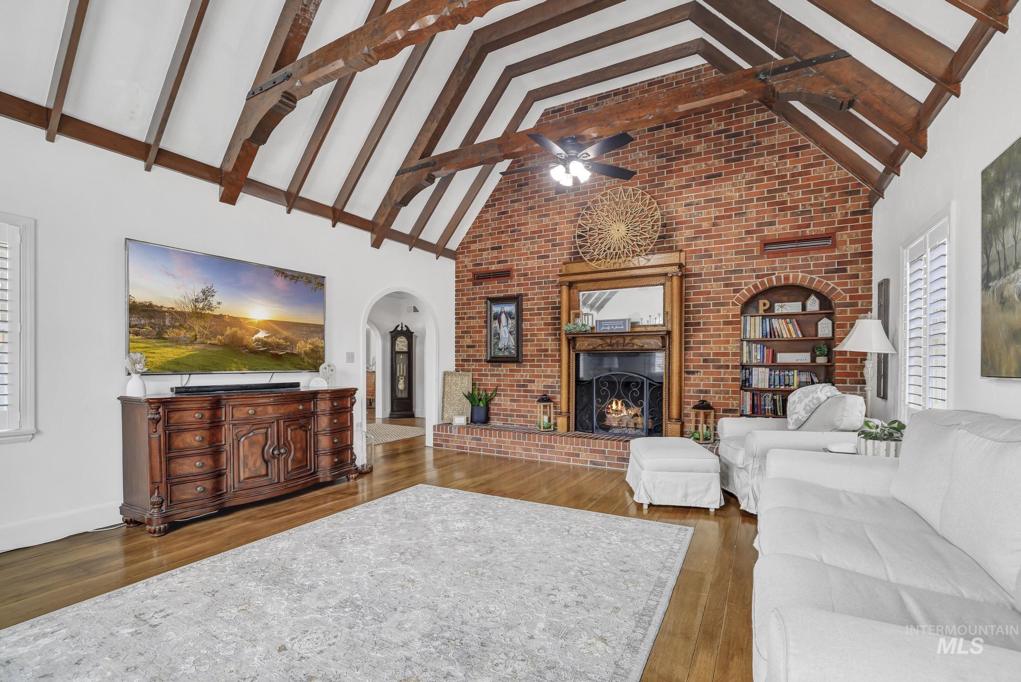 102 Fillmore Street Twin Falls, ID 83301 - Photo 11 of 48 Living area featuring a ceiling fan, a brick fireplace, dark wood-type flooring, arched walkways, and brick wall