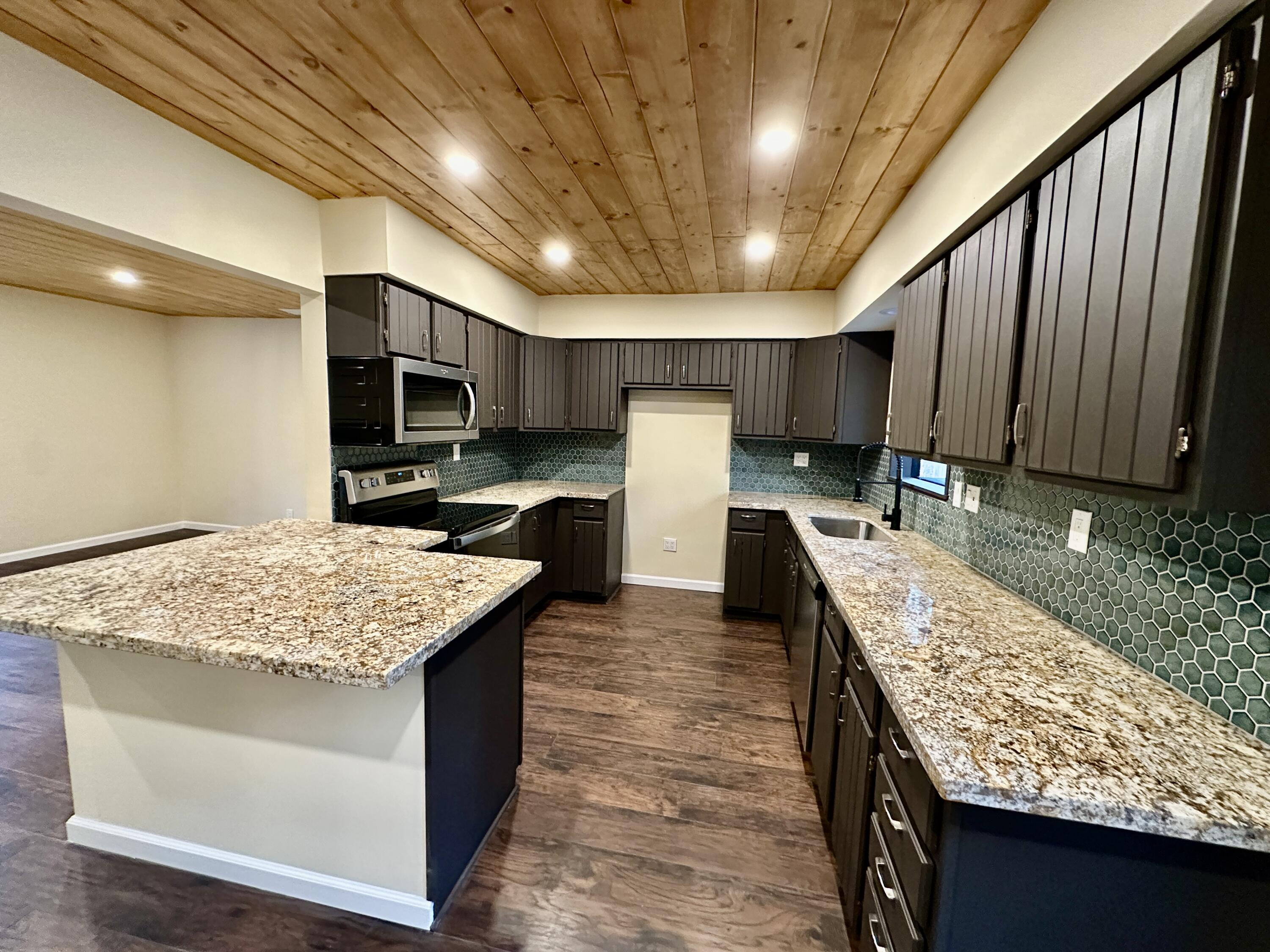 25340 Marion Ridge Drive Idyllwild, CA 92549 - Photo 8 of 31 a kitchen with kitchen island granite countertop wooden cabinets a sink dishwasher and a stove with wooden floor
