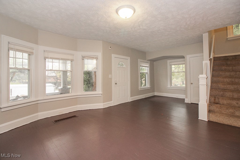 3085 Somerton Road Cleveland, OH 44118 - Photo 6 of 16 Unfurnished living room with visible vents, baseboards, stairs, arched walkways, and dark wood-style flooring