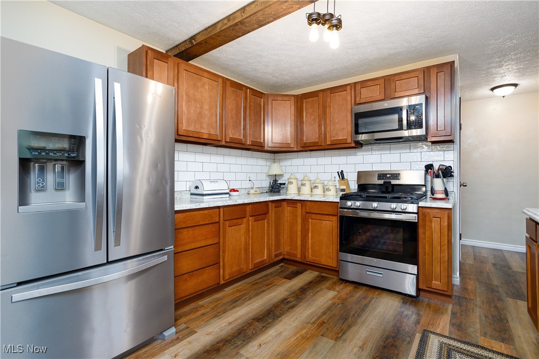 1153 Krumroy Road Akron, OH 44306 - Photo 13 of 26 Kitchen featuring appliances with stainless steel finishes, decorative backsplash, dark hardwood / wood-style floors, beamed ceiling, and a textured ceiling