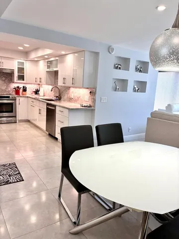 a kitchen with stainless steel appliances kitchen island granite countertop a table chairs sink and white cabinets