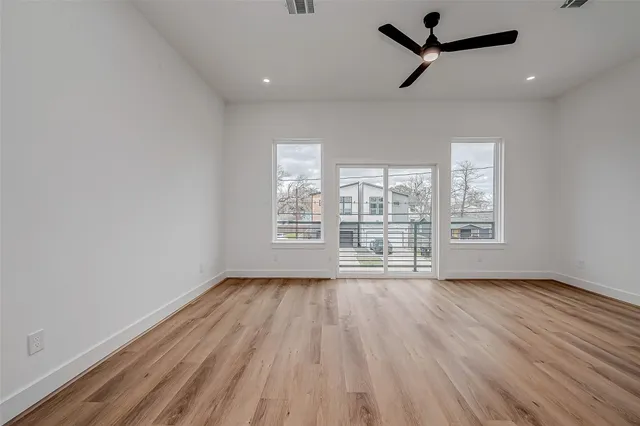 an empty room with wooden floor fan and windows