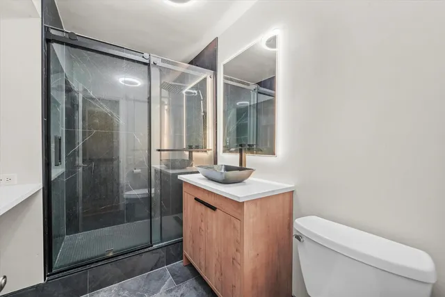 a bathroom with a granite countertop sink a toilet a mirror and shower