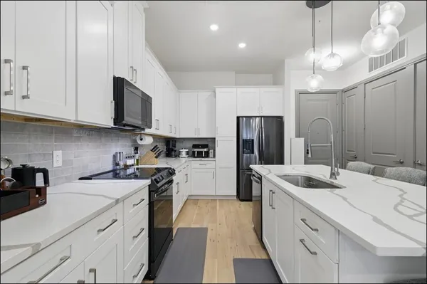 a kitchen with stainless steel appliances granite countertop a sink a stove a refrigerator cabinets and a dining table with wooden floor