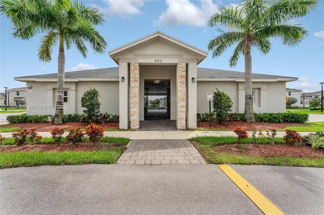a front view of a house with a garden and palm trees