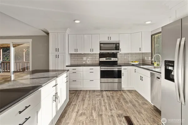 a open kitchen with stainless steel appliances granite countertop a stove top oven a sink and white cabinets