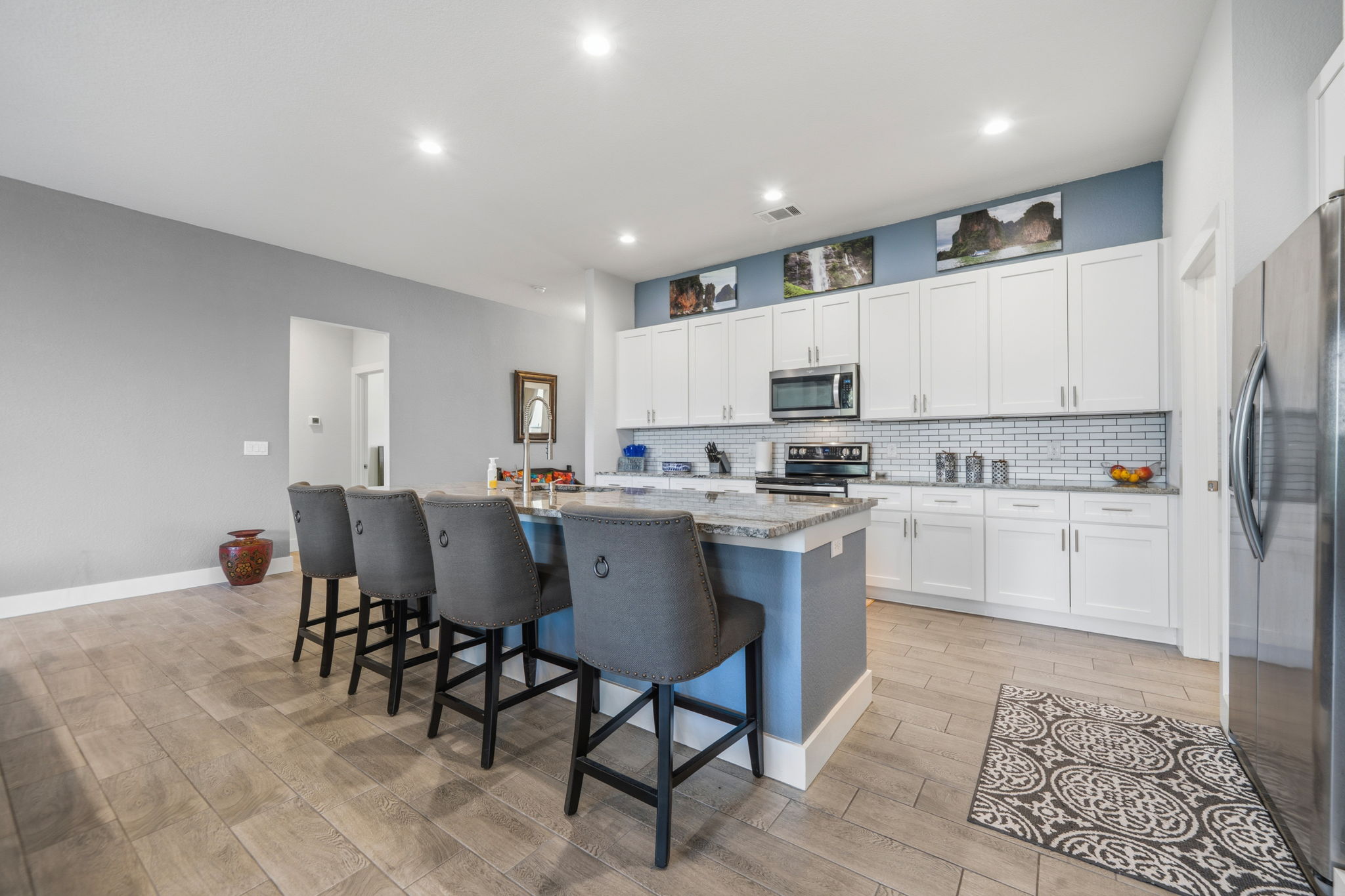 18605 Masters Cove Point Venture, TX 78645 - Photo 8 of 40 Open-concept kitchen featuring an island with seating, stainless steel appliances, white cabinetry, a subway tile backsplash, and wood-finish flooring