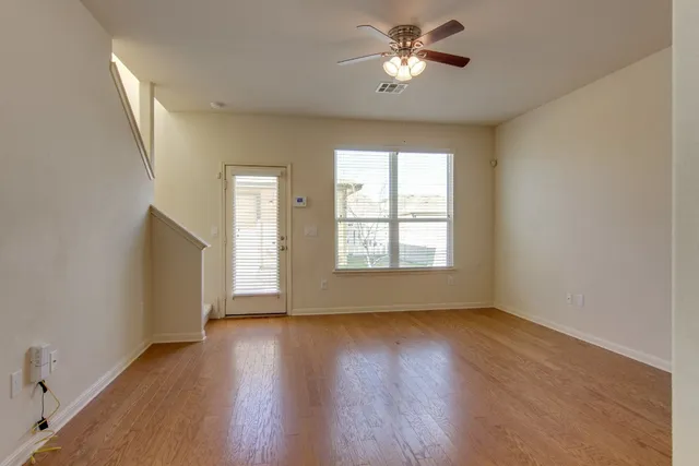 an empty room with wooden floor chandelier fan and windows