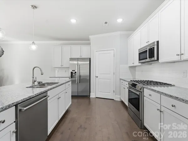 a kitchen with stainless steel appliances granite countertop white cabinets a sink a stove a refrigerator and a microwave