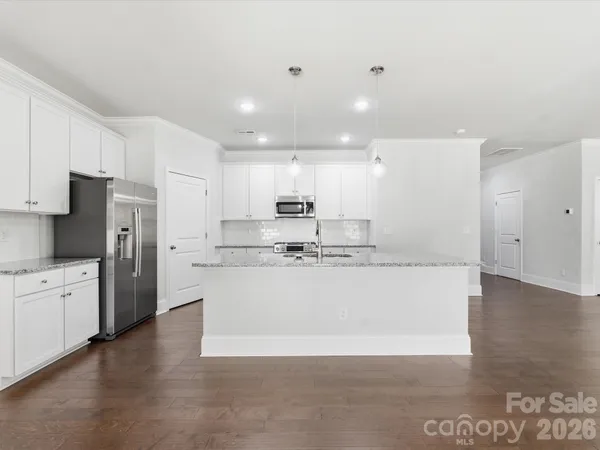 a large kitchen with stainless steel appliances granite countertop a stove a sink a refrigerator and white cabinets with wooden floor