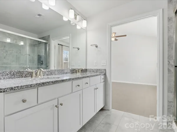 a bathroom with a granite countertop sink two mirror and a shower