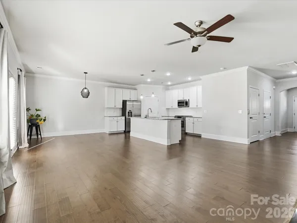 a view of an empty room with wooden floor and a ceiling fan