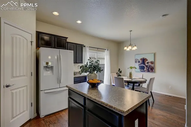 a kitchen with granite countertop a refrigerator a sink a dining table and chairs