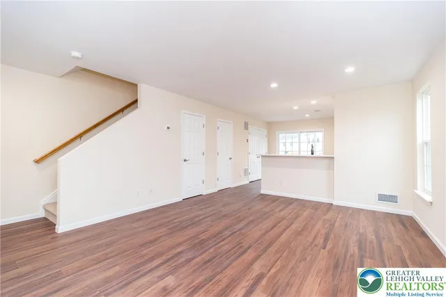 a view of empty room with wooden floor and kitchen
