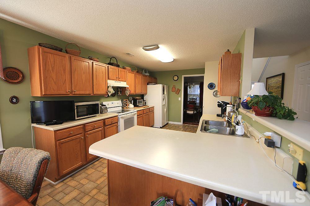 4707 Drewbridge Way Raleigh, NC 27604 - Photo 12 of 28 a kitchen with stainless steel appliances a sink a stove a refrigerator cabinets and a dining table with wooden floor