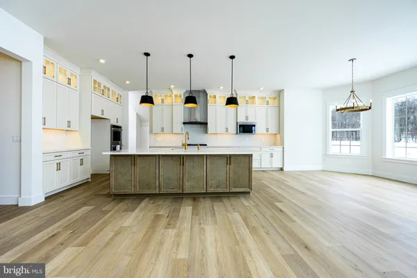 a large white kitchen with stainless steel appliances kitchen island granite countertop a stove a sink dishwasher and white cabinets with wooden floor