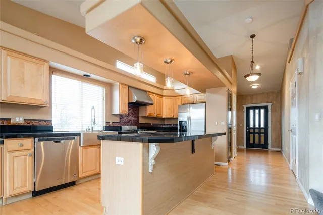 a kitchen with stainless steel appliances granite countertop a refrigerator a sink dishwasher a stove and white cabinets with wooden floor