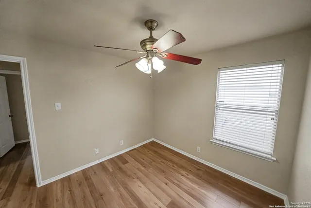 a big room with wooden floor a chandelier fan and windows