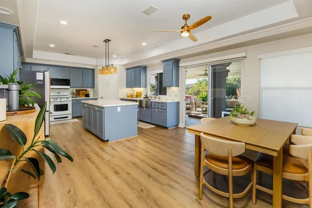 a kitchen with stainless steel appliances a stove a refrigerator a kitchen island a dining table and chairs with wooden floor