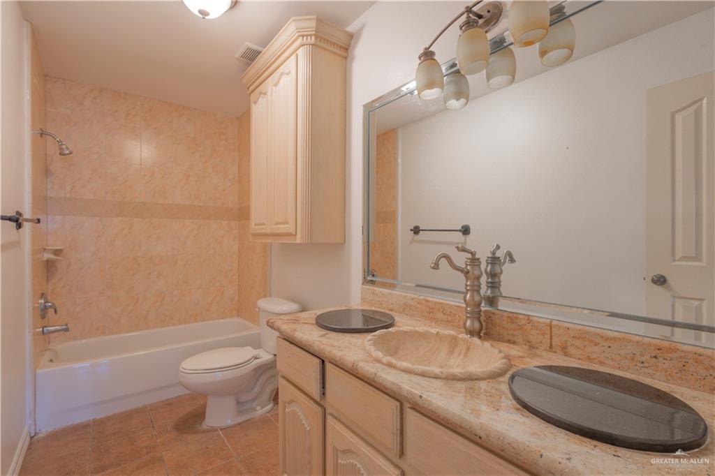 3909 Tulipan Street Mission, TX 78573 - Photo 14 of 16 a bathroom with a granite countertop sink a toilet a mirror and shower