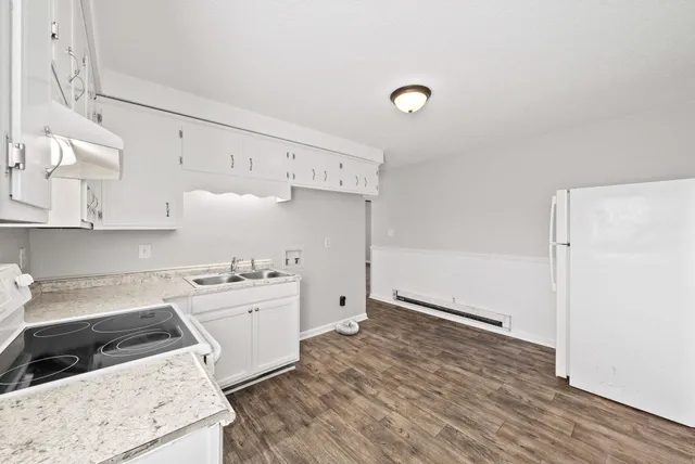 a kitchen with a stove a refrigerator and white cabinets with wooden floor