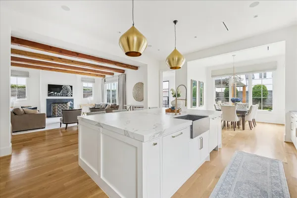 a large white kitchen with a large island oven a stove a sink a dining table and chairs with wooden floor