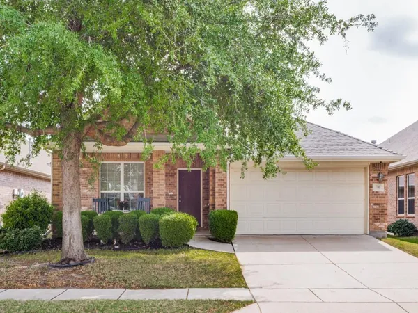 a view of a house with brick walls plants and large tree