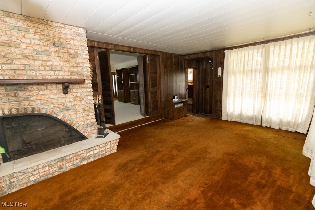 7312 Ivandale Road Independence, OH 44131 - Photo 17 of 44 Unfurnished living room featuring carpet, wooden walls, a brick fireplace, and brick wall