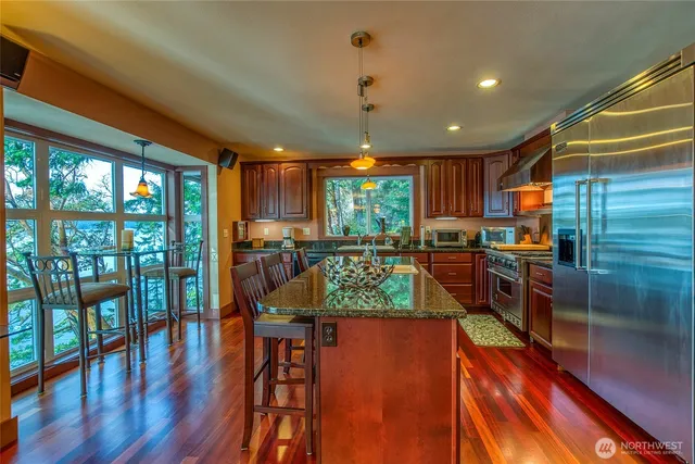 a kitchen with stainless steel appliances granite countertop a refrigerator a sink dishwasher a stove and a dining table with wooden floor