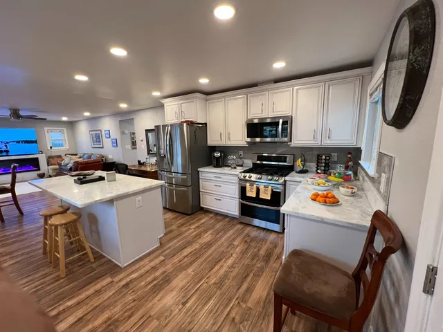 a kitchen with stainless steel appliances a stove a sink a refrigerator white cabinets and wooden floor