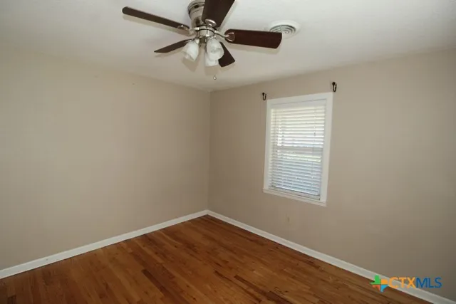 an empty room with wooden floor fan and windows