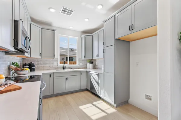 a kitchen with stainless steel appliances granite countertop a refrigerator a sink dishwasher and white cabinets with wooden floor