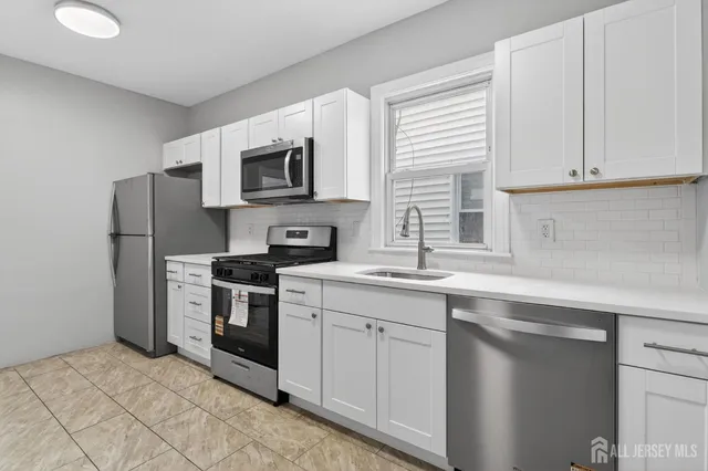 a kitchen with stainless steel appliances granite countertop white cabinets a sink a stove a refrigerator and a microwave