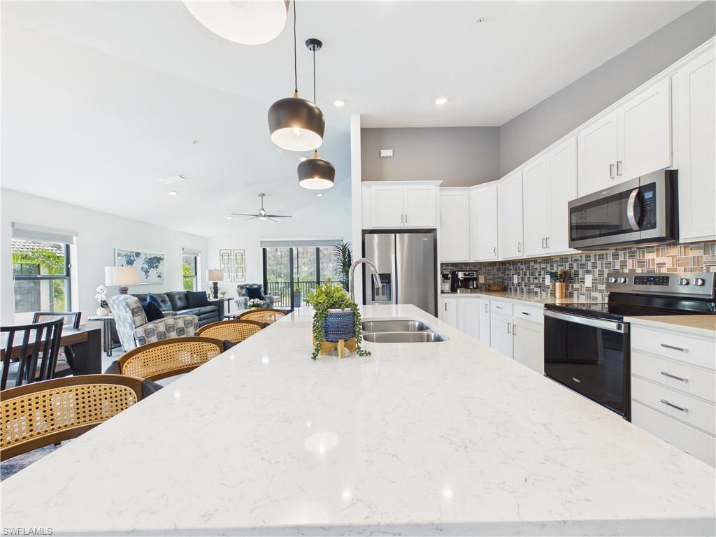 5683 Mayflower Way, Unit 908 Ave Maria, FL 34142 - Photo 9 of 37 Kitchen with stainless steel appliances, decorative light fixtures, white cabinetry, tasteful backsplash, and light stone countertops