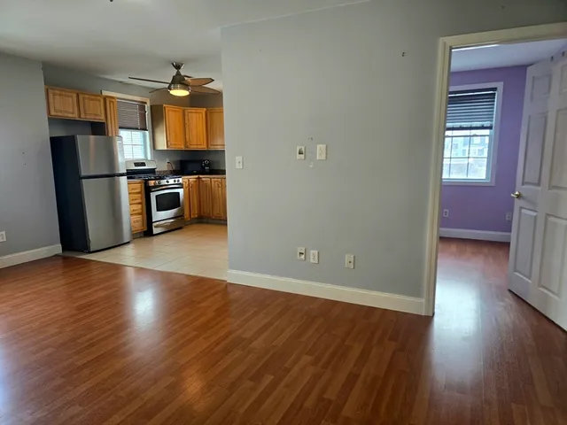 an empty room with wooden floor and a kitchen